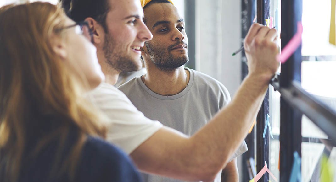 three people working at a whiteboard