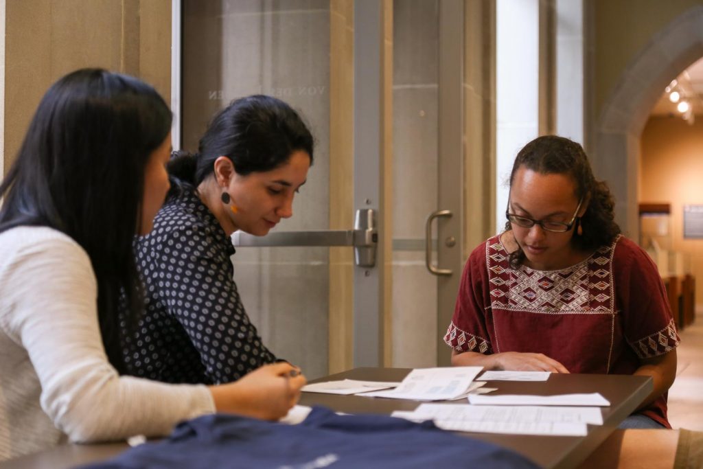 Three women talking over papers at a desk.