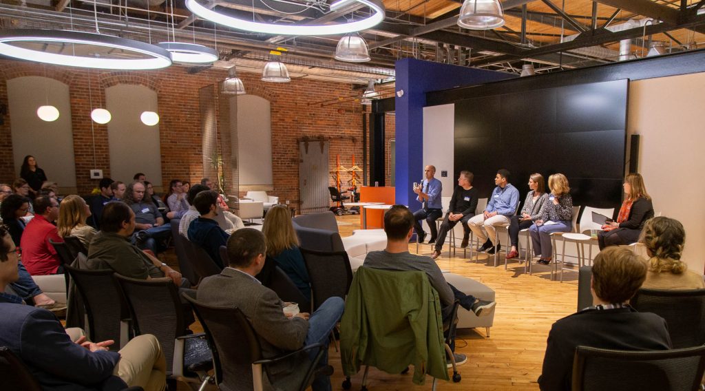A panel of speakers sit in front of a seated crowd.